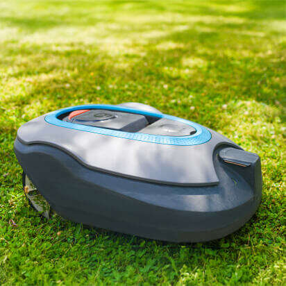 Ein Mähroboter steht auf grünem Gras, umgeben von blühenden Bäumen und Sonnenlicht.