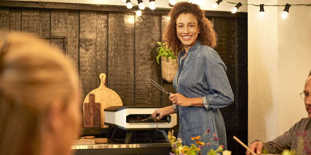 frau steht am pizzaofe cozze 1000x500